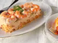Delicioso pudin de pescado cubierto con crema y camarones, decorado con perejil.