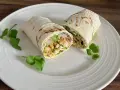 Kebab w tortilli przekrojony na pół, z kurczakiem, warzywami i kolendrą na białym talerzu.