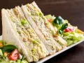 Sándwich de pollo cortado en triángulos, relleno de pollo desmenuzado y lechuga, acompañado de ensalada fresca.