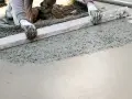 Ręce w rękawiczkach wyrównują świeży beton na taras za pomocą łaty.