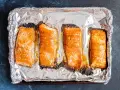 Cztery kawałki łososia pieczone na folii aluminiowej, gotowe do przygotowania sushi.