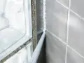 En fogpistol applicerar ny silikonfog längs en vägg av grå kakelplattor och glasblock.
