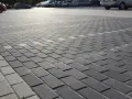Szary parking wyłożony kostką brukową holland. W tle widać zaparkowane samochody.