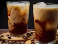 Två glas med iskaffe, där grädden virvlar i det mörka kaffet. Kaffebönor sprider sig runt glasen.