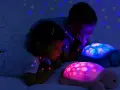 Dzieci zachwycone lampką projektorem dla dzieci w kształcie żółwia, która rzuca na ścianę kolorowe gwiazdki.