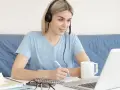 Pielęgniarka słucha wykładu na słuchawkach i notuje. Dostępne są darmowe kursy online dla pielęgniarek.