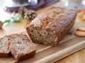 Un délicieux cake banane, coupé en tranches, sur une planche en bois. Des noix et des biscuits complètent cette gourmandise.