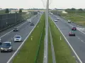 Na tej drodze szybkiego ruchu ruch jest umiarkowany. Widać kilka samochodów osobowych i jeden van. Po lewej stronie drogi znajduje się wysoki ekran akustyczny.
