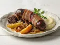 Pyszna kaszanka z piekarnika, owinięta boczkiem, podana z jabłkami i puree.