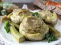 Carciofi alla romana cotti a puntino, teneri e saporiti, guarniti con menta fresca su un piatto bianco.