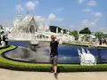 Mężczyzna pozuje przed olśniewającą białą świątynią Wat Rong Khun w Chiang Rai.