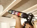 Uso di una pistola per colla per fissare il cartongesso a una struttura in legno.