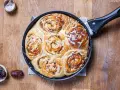 Frisch gebackene Zimtschnecken mit Apfelstückchen und Zuckerguss in einer Pfanne. Ein köstliches Apfel Zimtschnecken Rezept zum Nachbacken.