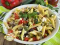 Pasta fredda con feta, peperoni, zucchine, melanzane e olive nere. Un piatto estivo colorato e saporito.