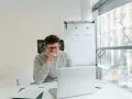 Mężczyzna w okularach siedzi przy biurku, zamyślony nad laptopem. Zastanawia się, kiedy należy się odprawa, analizując dokumenty.