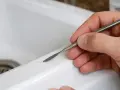 Main d'une personne utilisant un outil pour réparer une rayure sur un lavabo blanc.
