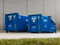 Dwa niebieskie kontenery BYS Recykling stoją przed budynkiem. Dowiedz się, ile kosztuje tona gruzu betonowego i jak go zamówić.