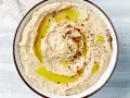 Kremowy, gładki hummus polany oliwą i posypany przyprawami. Idealny do maczania pieczywa.