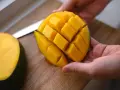Hände halten ein perfekt geschnittenes Mango-Viertel, bereit zum Genießen. Das Fruchtfleisch ist in Würfel geschnitten, was das Mango schneiden erleichtert.