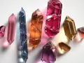 Cristales facetados de diversos tipos de cuarzo: rosa, azul, naranja, fucsia, dorado y amatista, brillan sobre fondo blanco.