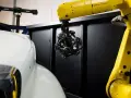 Robotyka i zaawansowany skaner optyczny badają kształt białego elementu, prawdopodobnie części samochodu.