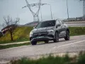 Szary Mercedes-Benz EQA jedzie po drodze, w tle linie energetyczne i drzewo.