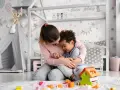 Ciepła opieka na dziecko w pokoju pełnym zabawek. Kobieta tuli chłopca, który opiera się o nią.