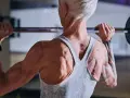 Stark ryggmuskulatur hos en kvinna som lyfter skivstång. Hon har tatuerade armar och en träningsklocka. För att bygga muskler är det viktigt med tillräckligt med gram protein per kg kroppsvikt.