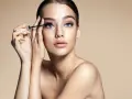 Donna con occhi azzurri applica mascara. Scopri come togliere il mascara waterproof senza irritare la pelle.
