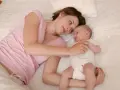 Mama patrzy z miłością na swoje 5 tygodniowe dziecko leżące obok niej na łóżku.