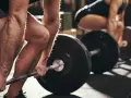 Personer lyfter skivstång i gym. Frågan "hur lång tid tar det att bygga muskler" besvaras med konsekvent träning.