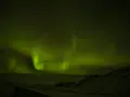 Niesamowita zorza polarna nad Islandią. Zielone smugi tańczą na nocnym niebie, oświetlając ośnieżony krajobraz i drogę.