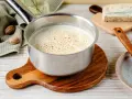 Cremige Gorgonzola-Sauce in einem Topf, bestreut mit Gewürzen. Daneben liegen Muskatnüsse und ein Stück Gorgonzola.