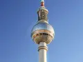 Die Torre della televisione di Berlino ragt in den blauen Himmel. Ihre kugelförmige Spitze mit Fenstern reflektiert das Licht.