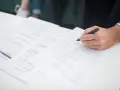 Ręka klienta podpisuje dokumenty ubezpieczeniowe. Agent ubezpieczeniowy czeka na zakończenie formalności.