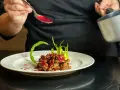 Chef decora un piatto di straccetti di manzo con una salsa rossa brillante, guarnendo con verdure verdi.