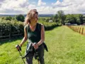 Donna sorridente con bastoncini da nordic walking, che lavora i muscoli coinvolti in un paesaggio verdeggiante.