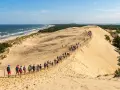Grupa turystów wędruje po piaszczystych wydmach w Słowińskim Parku Narodowym, podziwiając widok na morze i las.