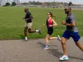 Trois personnes pratiquent un sport aérobie, courant sur un sentier pavé dans un parc verdoyant, avec une ligne d'horizon urbaine en arrière-plan.