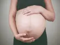 Dłońmi obejmuje zaokrąglony brzuch, czując delikatne ruchy dziecka w brzuchu.