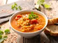 Eine dampfende Schüssel mit herzhafter rote linsensuppe, garniert mit Petersilie, daneben knuspriges Brot auf rustikalem Holztisch.