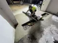 Pracownik wykonuje naprawę posadzki betonowej, wyrównując świeżą masę za pomocą łaty.