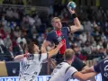 Dainis Kristopans w skoku rzuca piłką do bramki, otoczony przez obrońców.