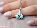 Un ciondolo con una splendida larimar pietra, incastonata con zirconi, adagiato su una mano con unghie lilla.