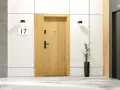 Drewniane drzwi wejściowe wewnętrzne z numerem 17, obok windy i schodów.