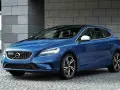 Niebieskie Volvo V40 D2 z czarnym dachem, zaparkowane na kamiennej nawierzchni, z nowoczesną architekturą w tle.