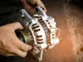Hände halten eine Lichtmaschine. Sie ist ein wichtiges Bauteil, das Strom erzeugt, damit das Auto fährt.
