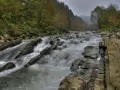 Bieszczady w jesiennej odsłonie. Rzeka wartko płynie wśród kamieni, tworząc sine wiry. Las na zboczu mieni się barwami.
