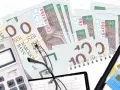 Zestaw do windykacji: banknoty, kalkulator, okulary i długopis. Bocian symbolizuje nadzieję na odzyskanie należności.
