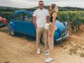 Couple souriant devant une 2CV bleue dans les vignes, une belle idée pour visiter Beaune en 1 jour.